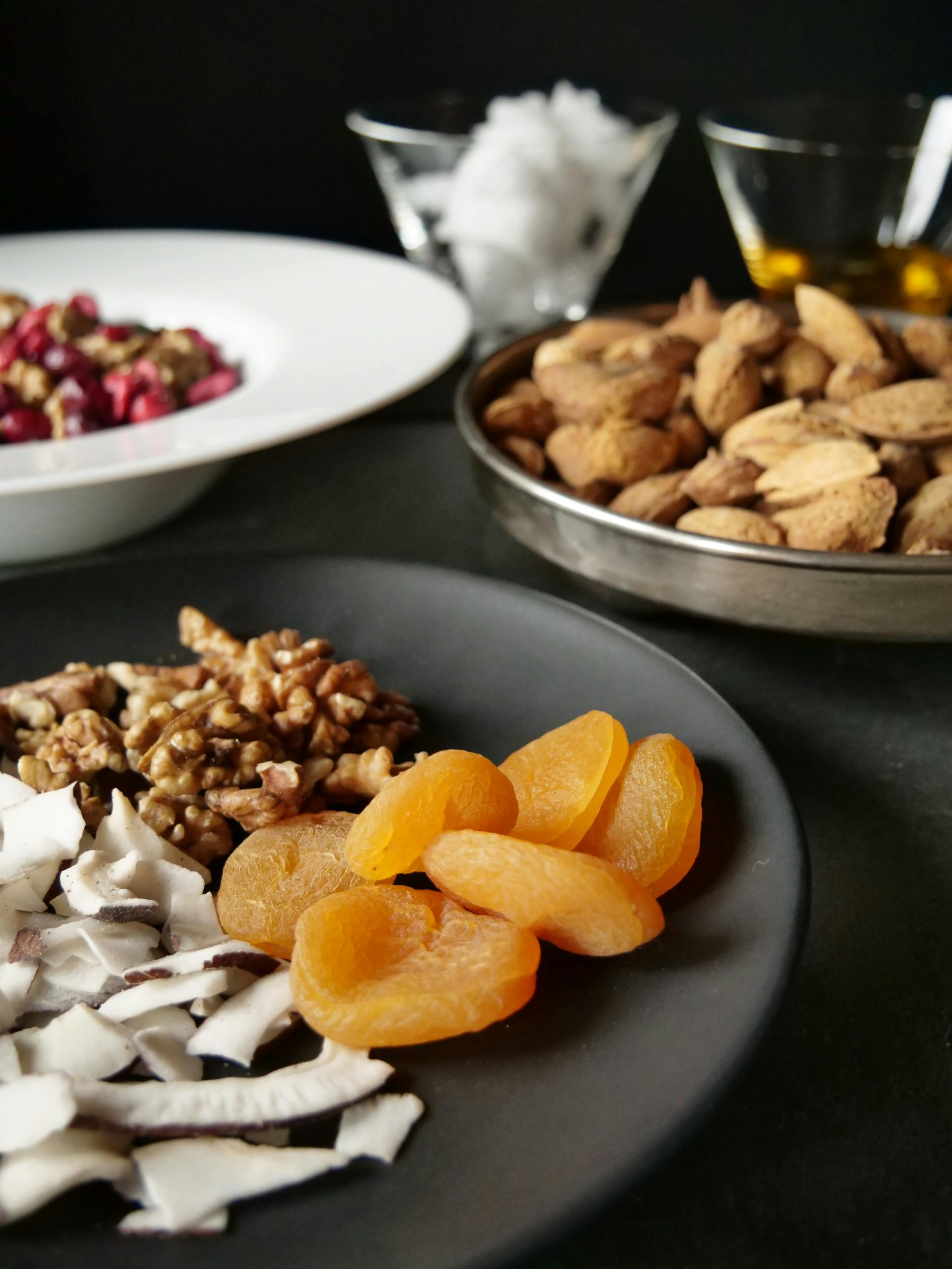 A close-up of nuts, dried apricots, and fruits on dark plates. Ideal for food photography.